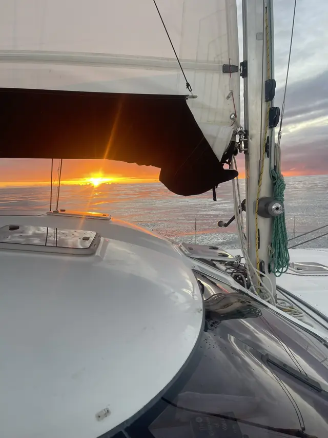 The sun setting through the sails and rig of Mā Tori mid-ocean