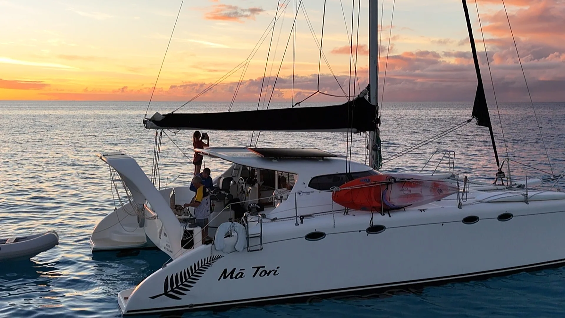 Mā Tori at anchor in Fiji at golden hour, silver fern and name on her bow, crew aboard as the sun sets